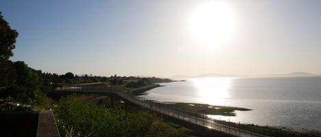 A coastal bridge with a clear view of the sea and distant mountains.