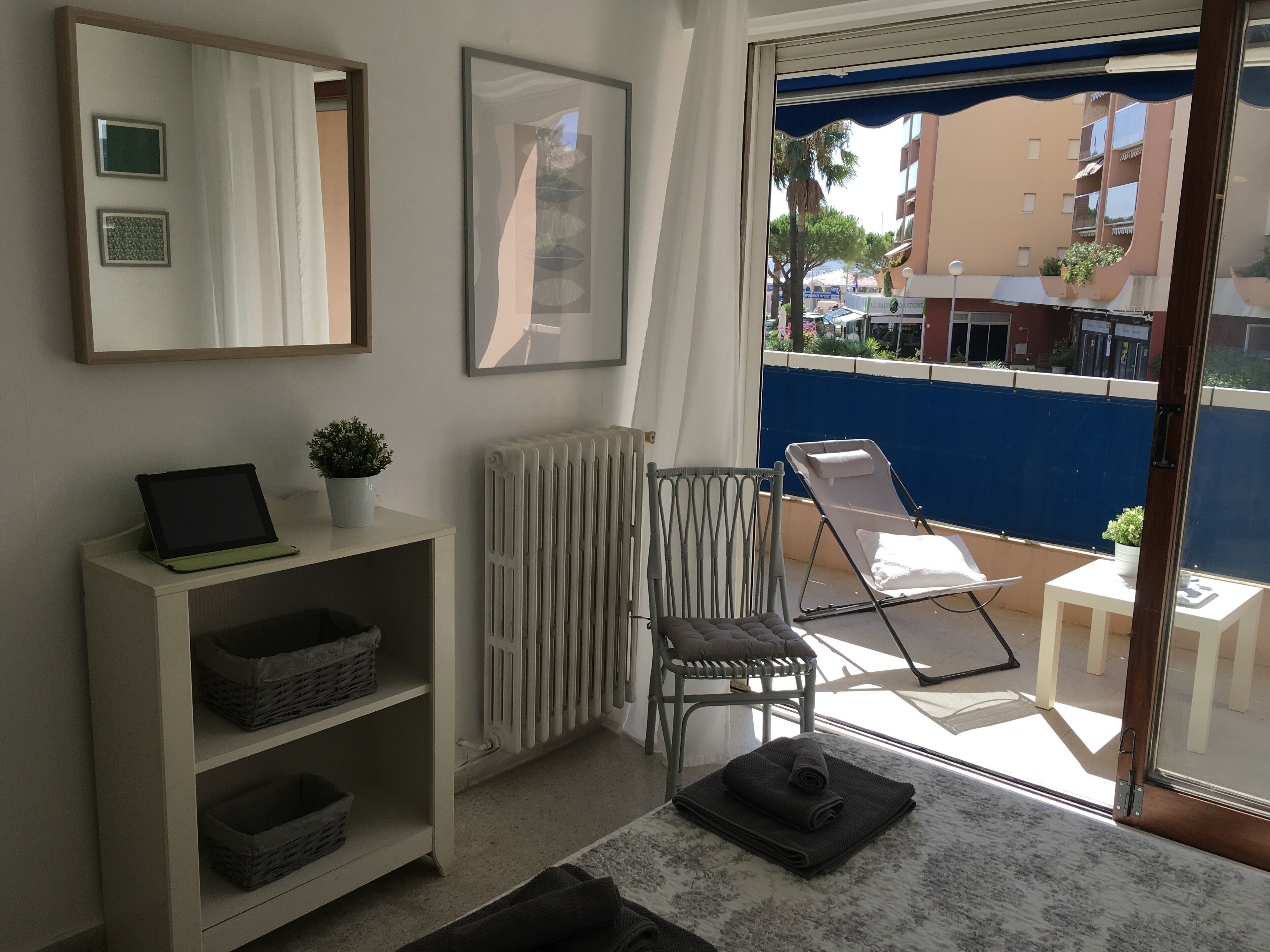 Un balcon avec une chaise, une table, un radiateur, une étagère avec des paniers et une plante en pot.