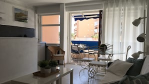 Un espace de vie compact comprenant un coin cuisine, un coin repas avec une table et des chaises, un canapé et une vue sur le balcon extérieur.
