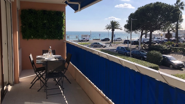 Un balcon avec une table dressée pour le dîner, une vue sur la mer et des voitures garées.