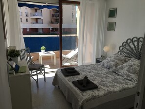A bedroom with a bed, a chair, a small table, and a view of the outside balcony. - Beautiful 2 bedroom apartment by the sea (4 pers) (Fréjus)