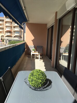 A balcony with a table, chairs, a potted plant, and a view of a building with balconies. - Beautiful 2 bedroom apartment by the sea (4 pers) (Fréjus)