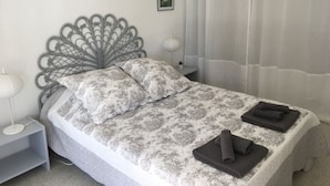 Un lit bien fait, avec une couvre-lit à motifs et des oreillers, une tête de lit décorative en métal, une lampe de chevet et une petite plante en pot posée sur une table de chevet.