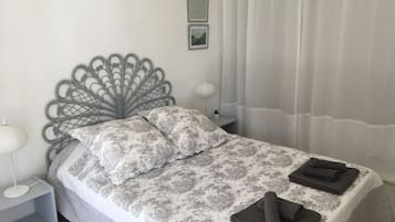 Un lit bien fait, avec une couvre-lit à motifs et des oreillers, une tête de lit décorative en métal, une lampe de chevet et une petite plante en pot posée sur une table de chevet.