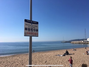 Escena de playa con un cartel que indica 'Ville de Fréjus' y 'Bienvenue sur la plage du Capitoule'.