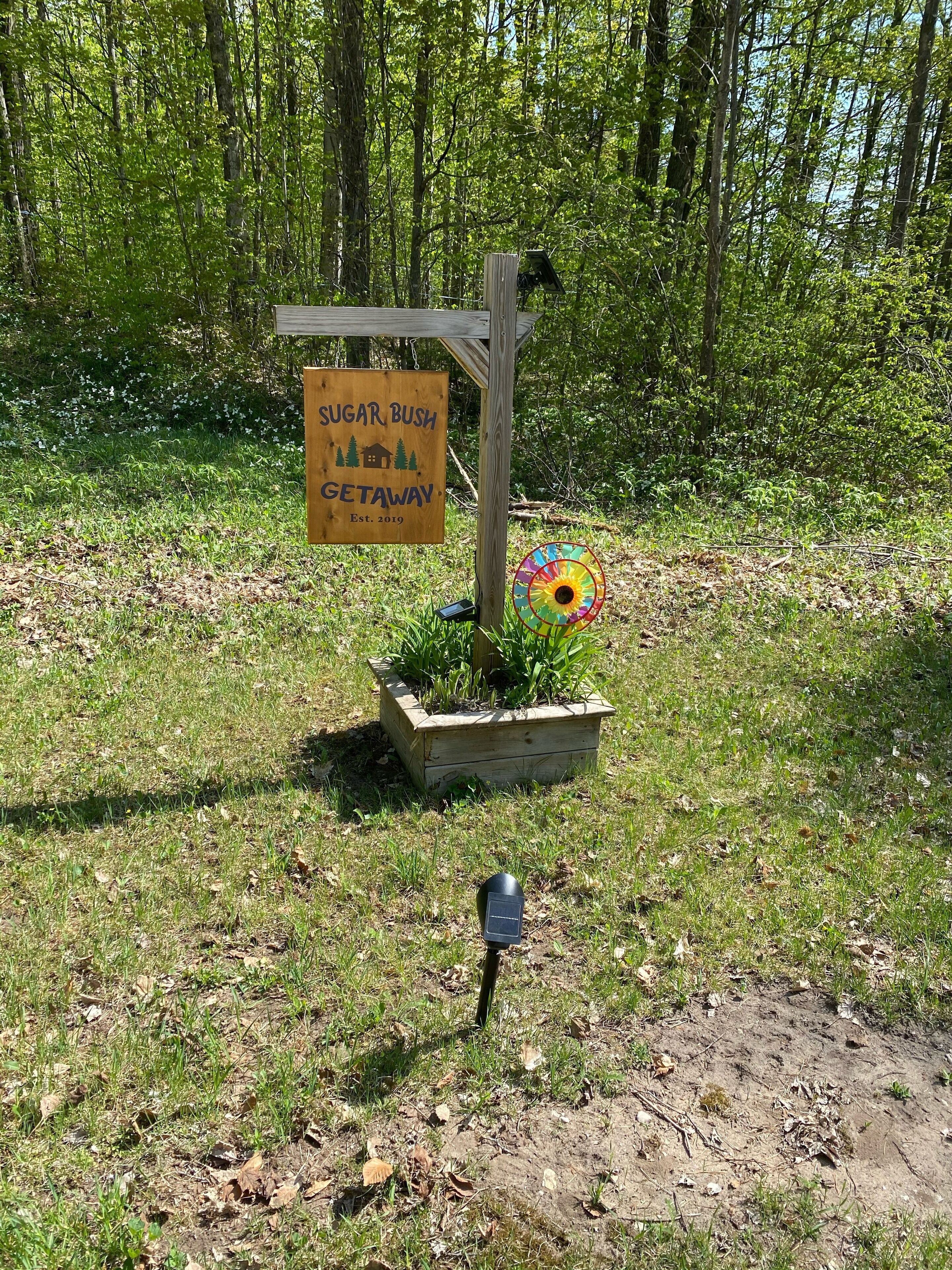 A wooden sign with the text "Sugar Bush Getaway" and a colorful windmill.