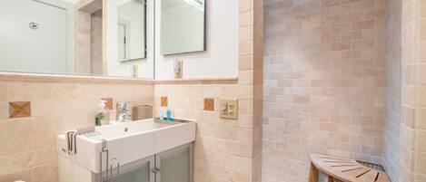 Baño con lavamanos, espejo y zona de ducha.