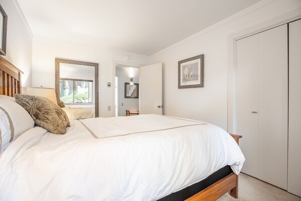 Een slaapkamer met een groot bed, een houten hoofdbord, een spiegel, een lijst met een afbeelding en een kledingkast.