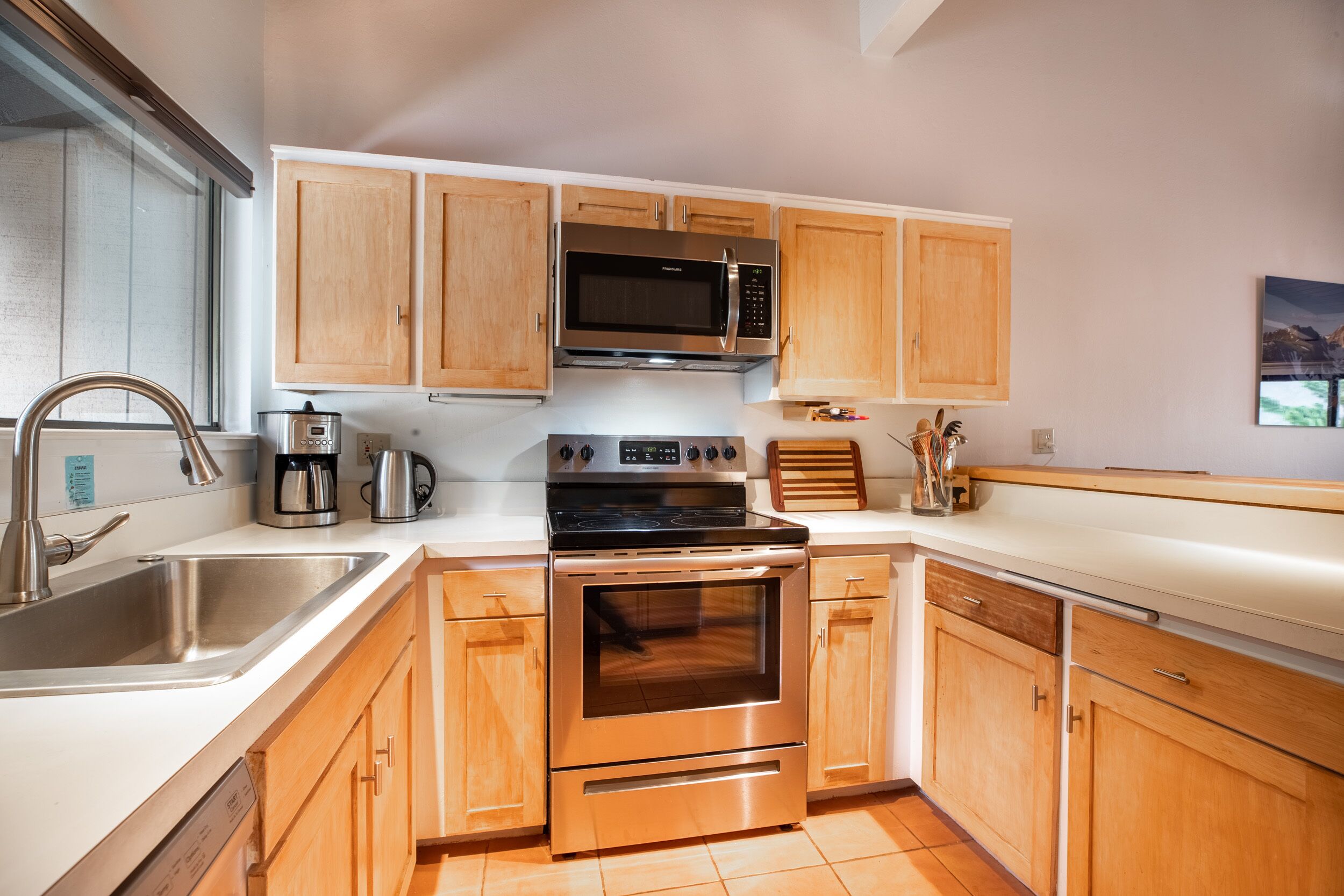 Una cocina con armarios de madera, electrodomésticos de acero inoxidable, microondas, cafetera y un lavamanos.