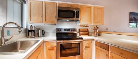 Una cocina con armarios de madera, electrodomésticos de acero inoxidable, microondas, cafetera y un lavamanos.