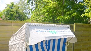 Een strandstoel met een gestreepte kussen en een wit zonnescherm, op een gazon.