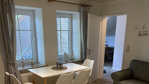 Een moderne woonkamer met een witte eettafel, vier witte stoelen, een grijze bank en een kleine salontafel.