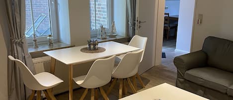 Una sala de estar moderna con una mesa de comedor blanca, cuatro sillas blancas, un sofá gris y una pequeña mesa de centro.