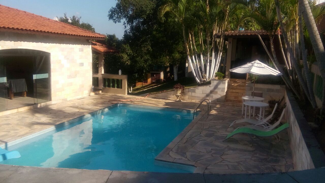 Una piscina con piastrelle in pietra, una zona relax coperta e un percorso alberato da palme.