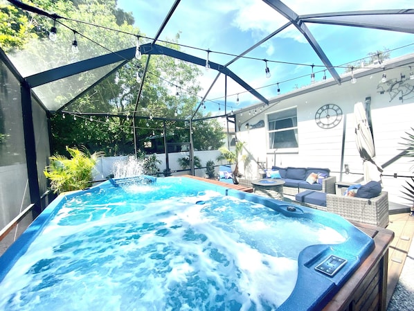 A hot tub with a glass enclosure, surrounded by outdoor furniture and a house in the background. - The Great Escape 3BR 2B Entire house (Tampa)