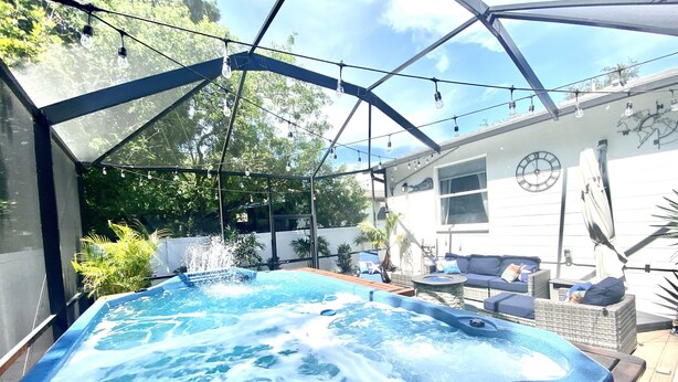 Un bain à remous doté d’une enceinte en verre, entouré de mobilier d’extérieur et avec une maison en arrière-plan.