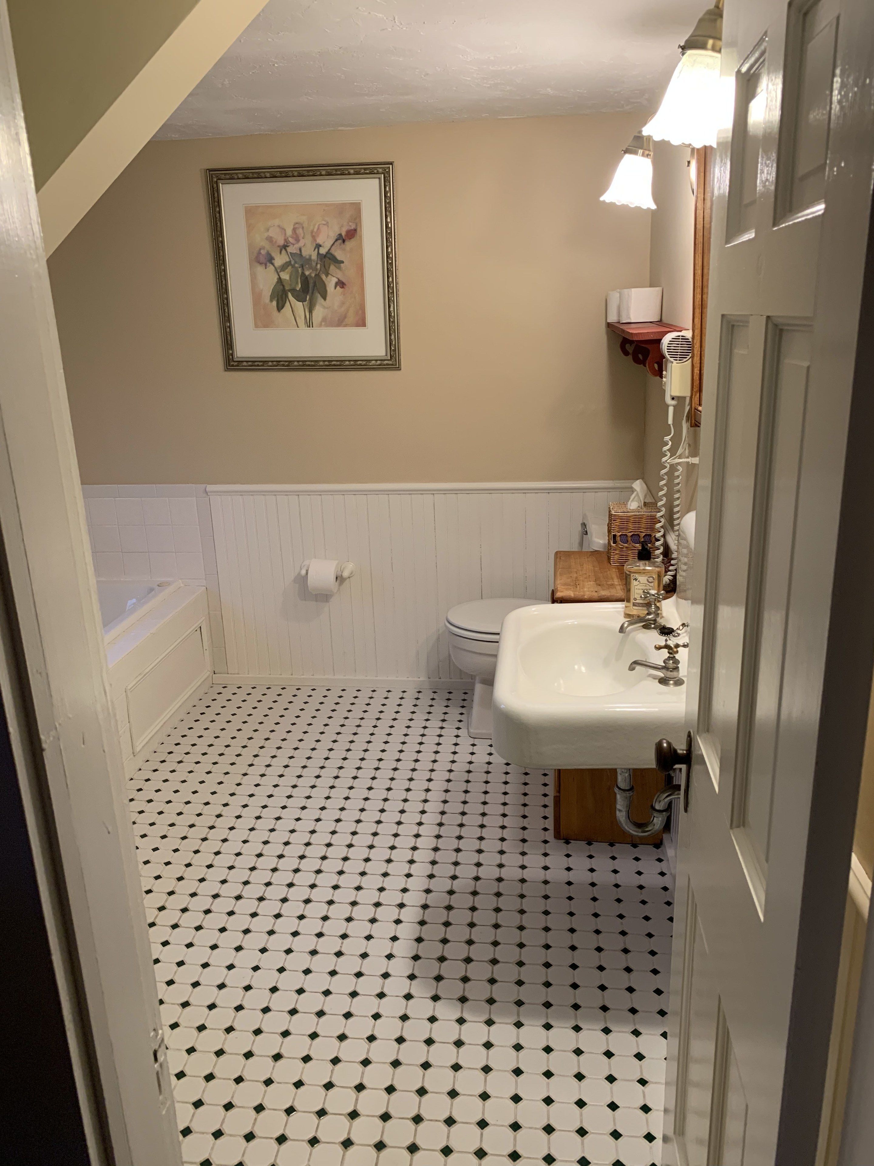 A bathroom with a white sink, toilet, and bathtub. There is a framed picture on the wall and a white radiator below the sink.