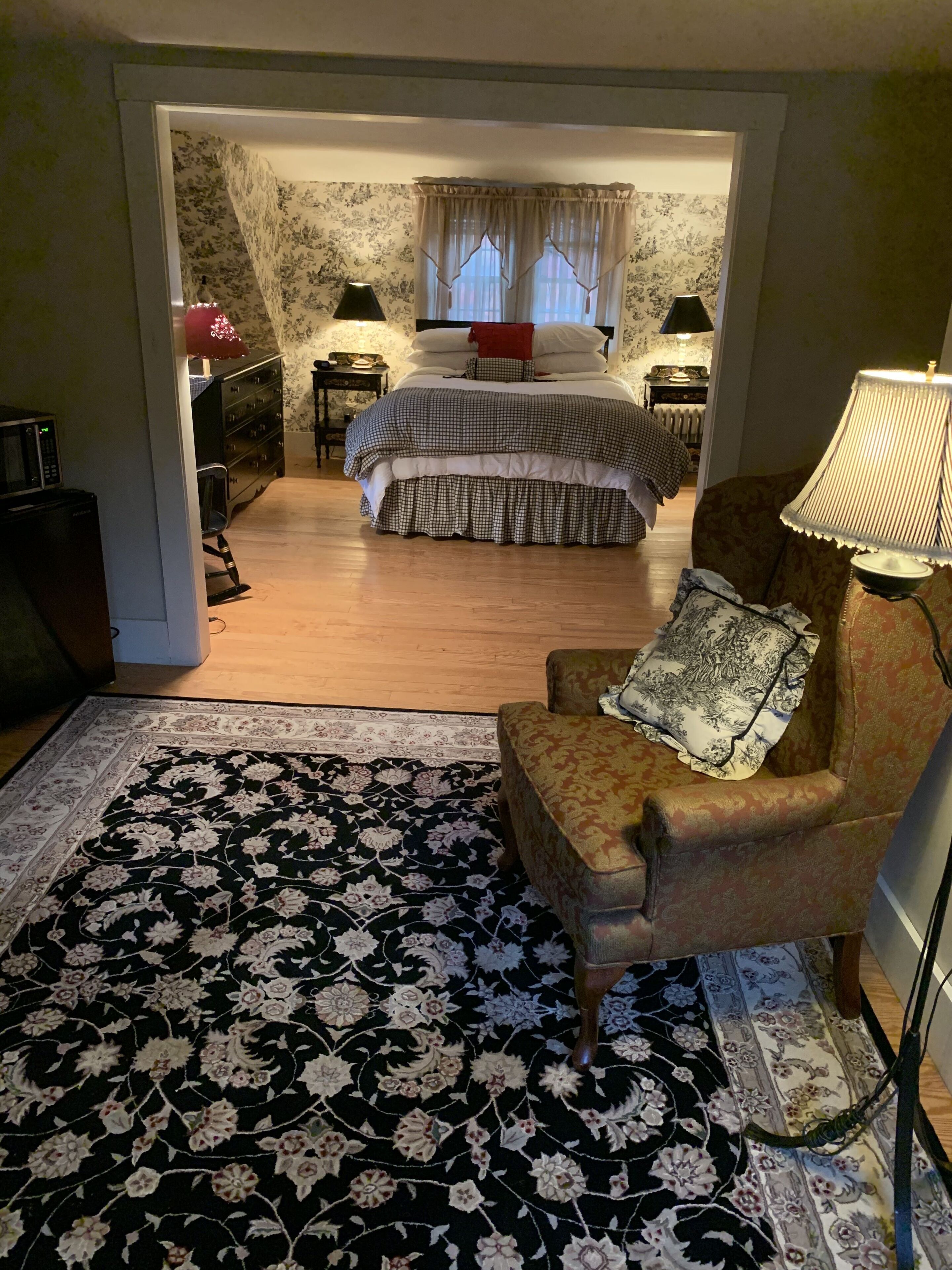 Un dormitorio con cama, una silla, una lámpara, una mesita de noche y un aparador.