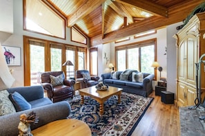 A spacious living room with a high ceiling, large windows, and a variety of seating options including a sofa, chairs, and a coffee table.