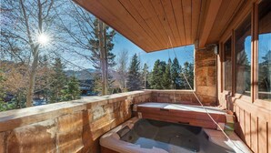 Un jacuzzi de madera con paredes de piedra, techo de madera y vistas a árboles y montañas.