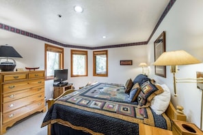 A bedroom with a bed, dresser, television, and two windows.
