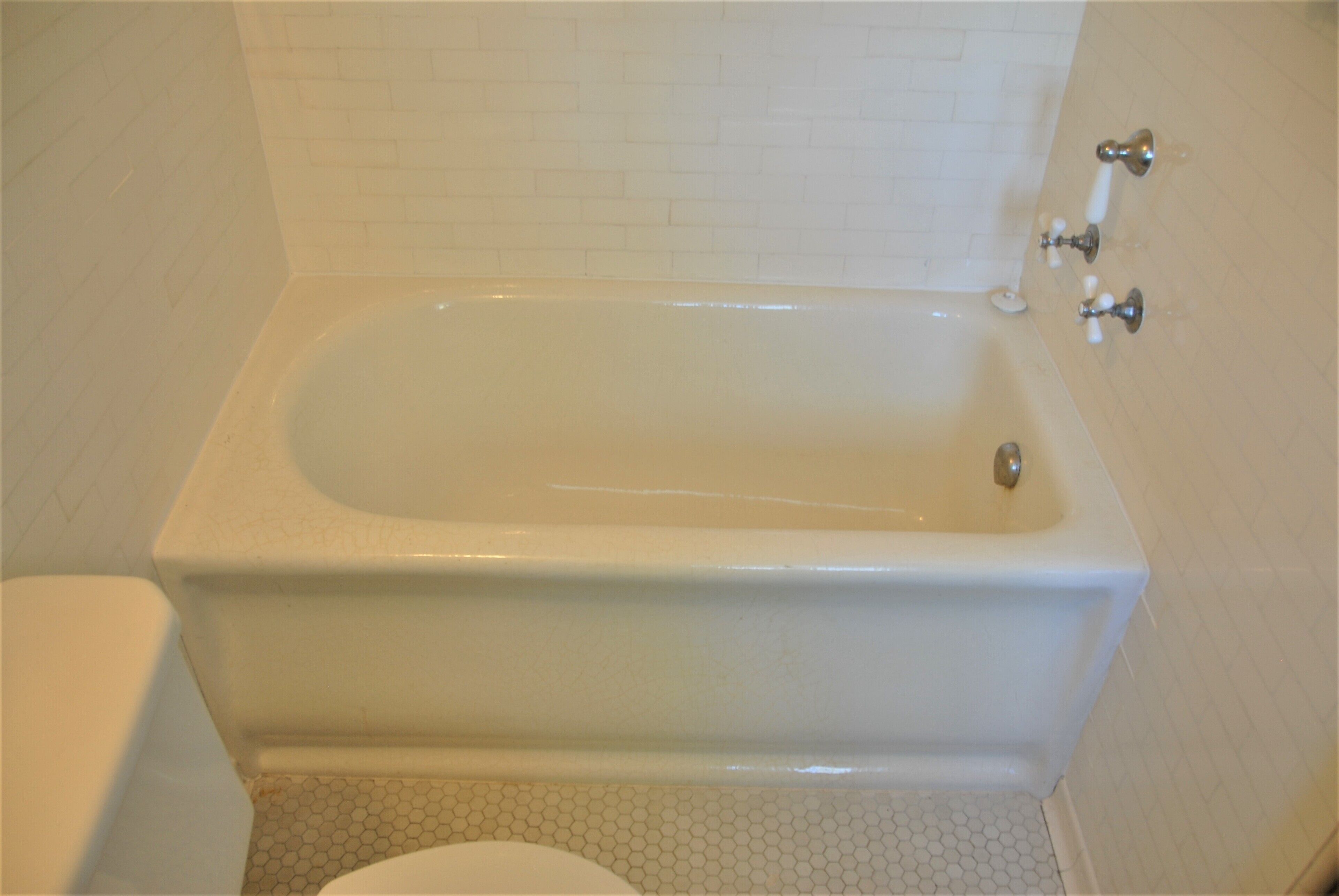 A bathroom with a bathtub, toilet, and a tiled floor.