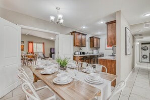 A dining area with a wooden table set for six, surrounded by white chairs. A kitchen is visible in the background with wooden cabinets and a countertop. - 🌞6 KING beds, 14 GUESTS, 5 BEDROOMS, 2 BATHROOMS, REFRIGERATION, NEAR AIRPORT (El Paso)