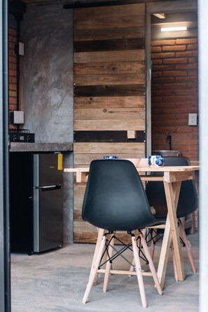Una cocina moderna con pared de madera, un refrigerador y dos sillas negras junto a una mesa de madera.