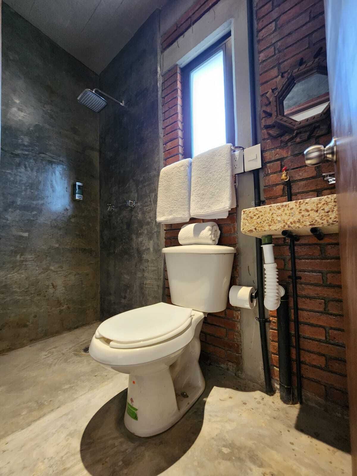 Une salle de bain avec des toilettes blanches, une douche et un lavabo avec un mur de fond en briques.