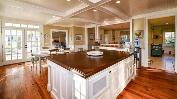 A spacious kitchen with a large island, wooden flooring, and a high ceiling with cross beams.