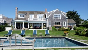 A large house with a swimming pool, a covered patio, and a well-maintained lawn.