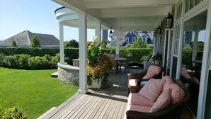 A covered outdoor area with a wooden deck, wicker furniture, and a stone wall.