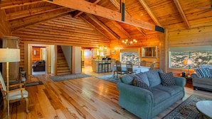 A spacious wooden cabin with a dining area, kitchen, and a large window offering a view of the outdoors.