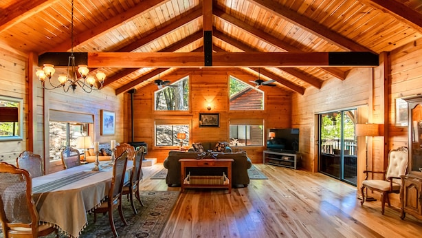 A spacious wooden cabin interior with a dining area, living room, and large windows providing natural light.