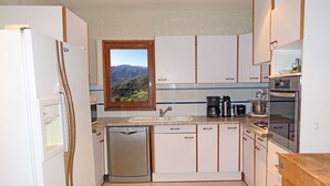 Cocina compacta con armarios blancos, lavavajillas integrado, cafetera y horno.