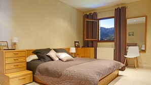 Un dormitorio con cama, cómoda de madera, mesitas de noche, un espejo y una ventana con cortinas.