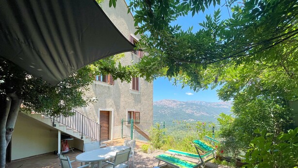 Un patio con mobiliario exterior, vistas a montañas y un edificio con balcones.