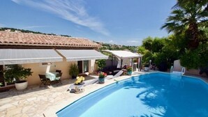 Ein Pool mit Fliesenverkleidung, ein überdachter Sitzbereich im Freien und ein Gebäude mit einem geflasten Dach.