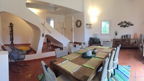 Ein großzügiger Essbereich mit einem langen Holztisch, Korbstühlen und einem einzigartigen Treppenhausdesign.