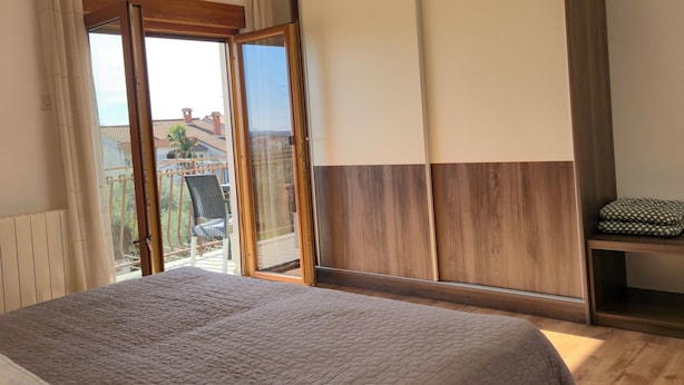 A bedroom with a large bed, a sliding door to a balcony, and a wardrobe.