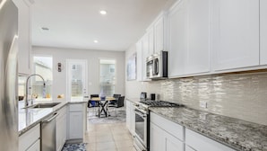 Una cocina moderna con gabinetes blancos, electrodomésticos de acero inoxidable y un salpicadero de azulejos.