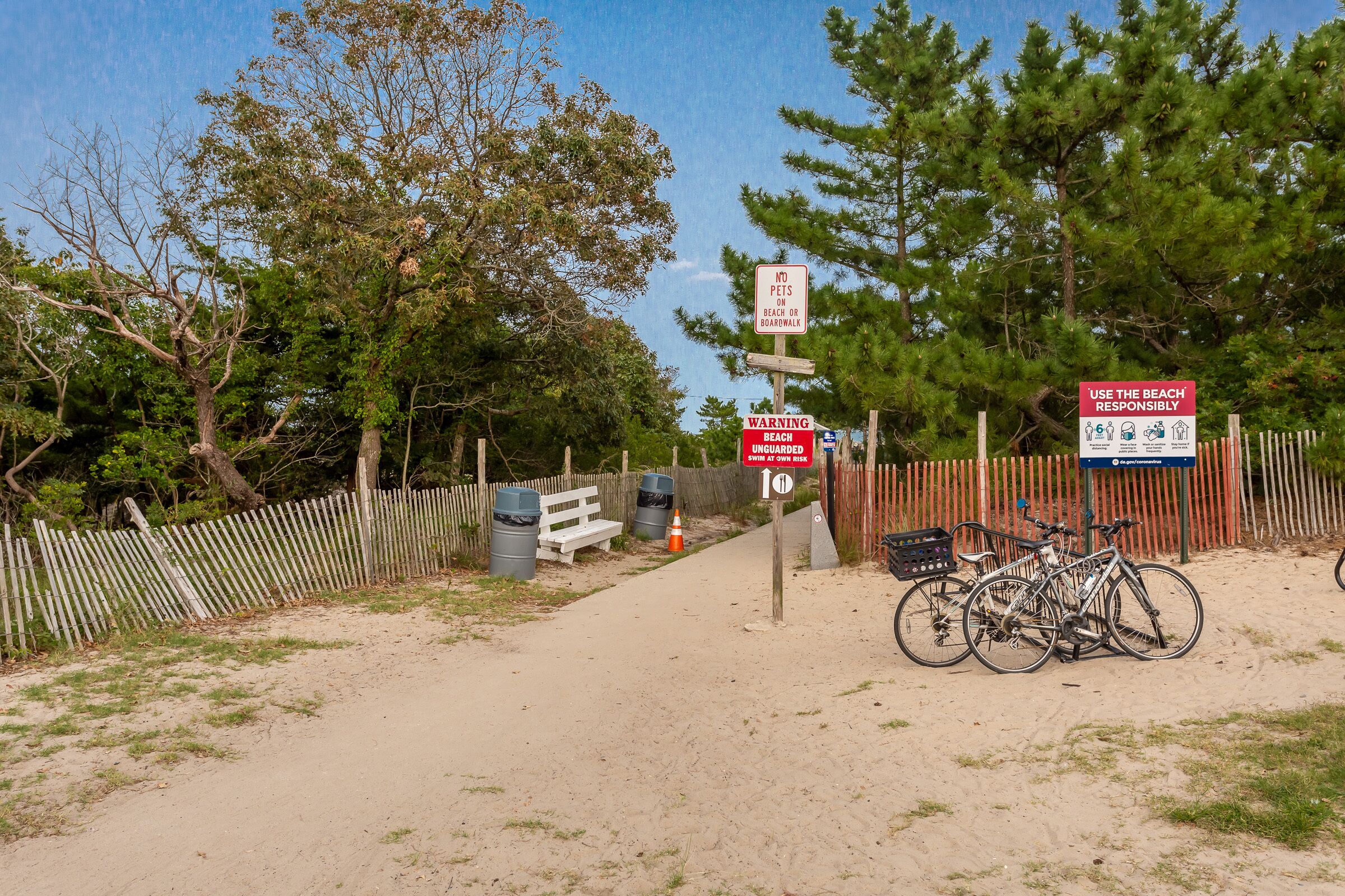 A beach entrance with a wooden fence, a sign prohibiting pets on the beach, and a warning sign about the beach being unguarded.