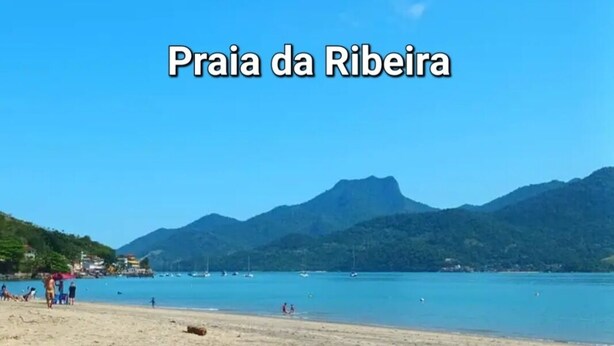Spiaggia di Ribeira con acque blu cristalline, montagne sullo sfondo e cielo sereno.