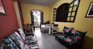 Una sala de estar con sofás estampados, un comedor con mesa y sillas, y un ventanal con contraventanas.