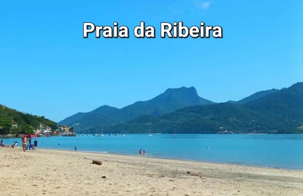 Playa Ribeira con aguas azules cristalinas, montañas al fondo y un cielo despejado.