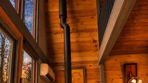 Ein gemütliches Zimmer mit Kaminofen, großen Fenstern und einem modernen Sessel.