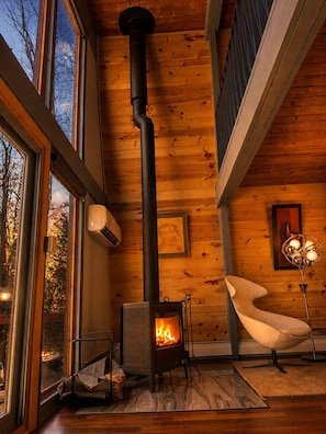 Une pièce chaleureuse avec un poêle à bois, de grandes fenêtres et un fauteuil moderne.