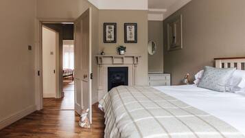A bedroom with a bed, a fireplace, a door leading to another room, and a hallway.