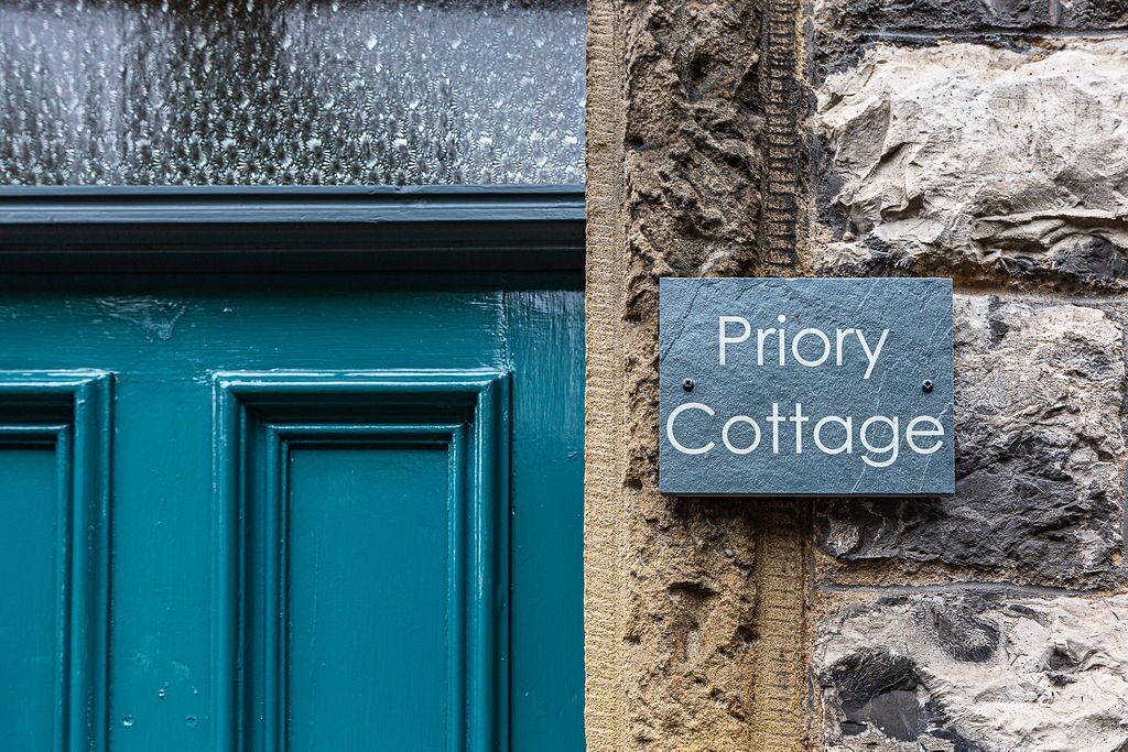 A teal door and a stone wall with a sign reading "Priory Cottage".