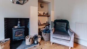 Una sala de estar acogedora con chimenea, un sillón cómodo y una estantería llena de libros y objetos decorativos.